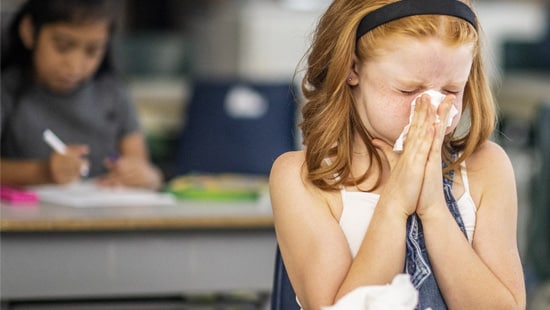 Young girl sneezing into a facial tissue