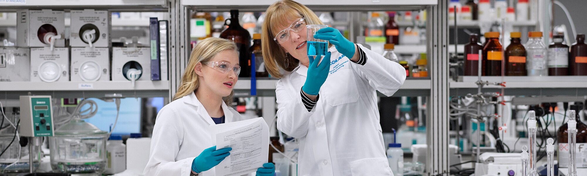 2 female Ecolab lab technicians looking at a vile of blue fluid