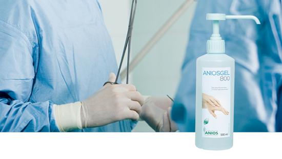 Bottle of ANIOSGEL 800 hand sanitizer with pump dispenser in foreground, and two medical professionals in blue surgical gowns and gloves in background.