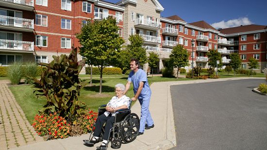 Elderly resident in a wheelchair escorted on a walk with a staff member in a long-term care community